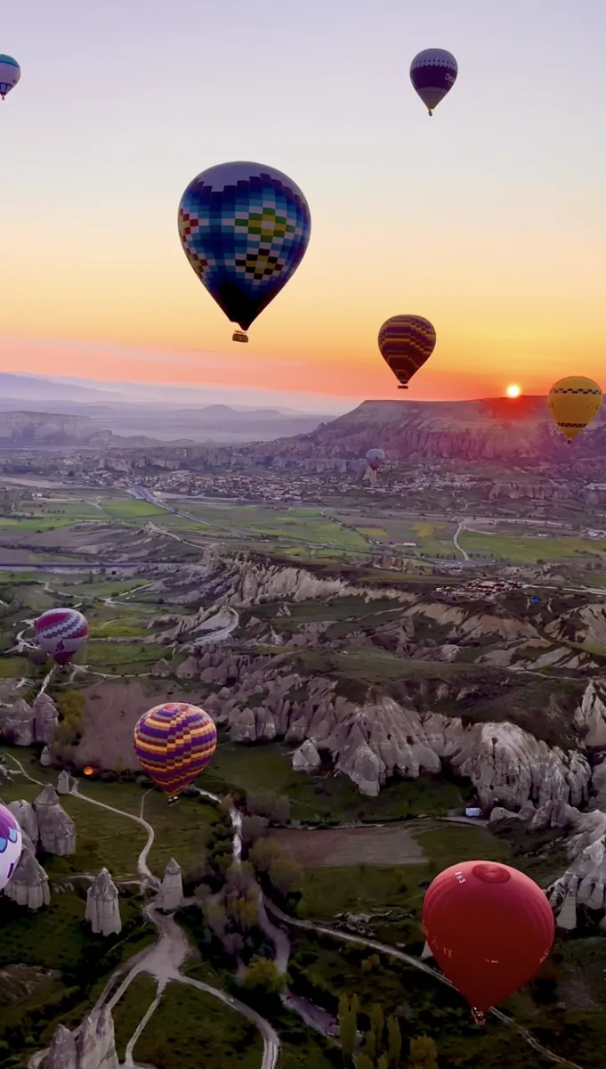 Hot air balloons flying over Cappadocia fairy chimneys at sunrise
