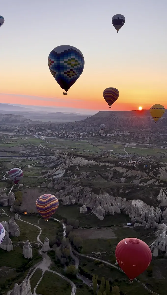 Dozens of hot air balloons over Cappadocia valleys seen from above at sunrise