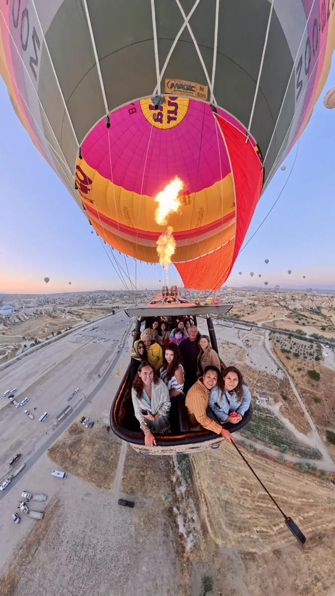 Happy guests in a hot air balloon basket with the burner flame lit over Cappadocia